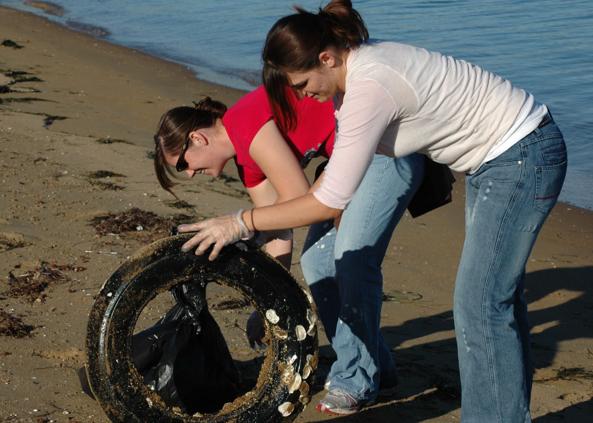 Two volunteers haul a barnacle-covered tire out of the water onto the sand during a San Diego shoreline cleanup