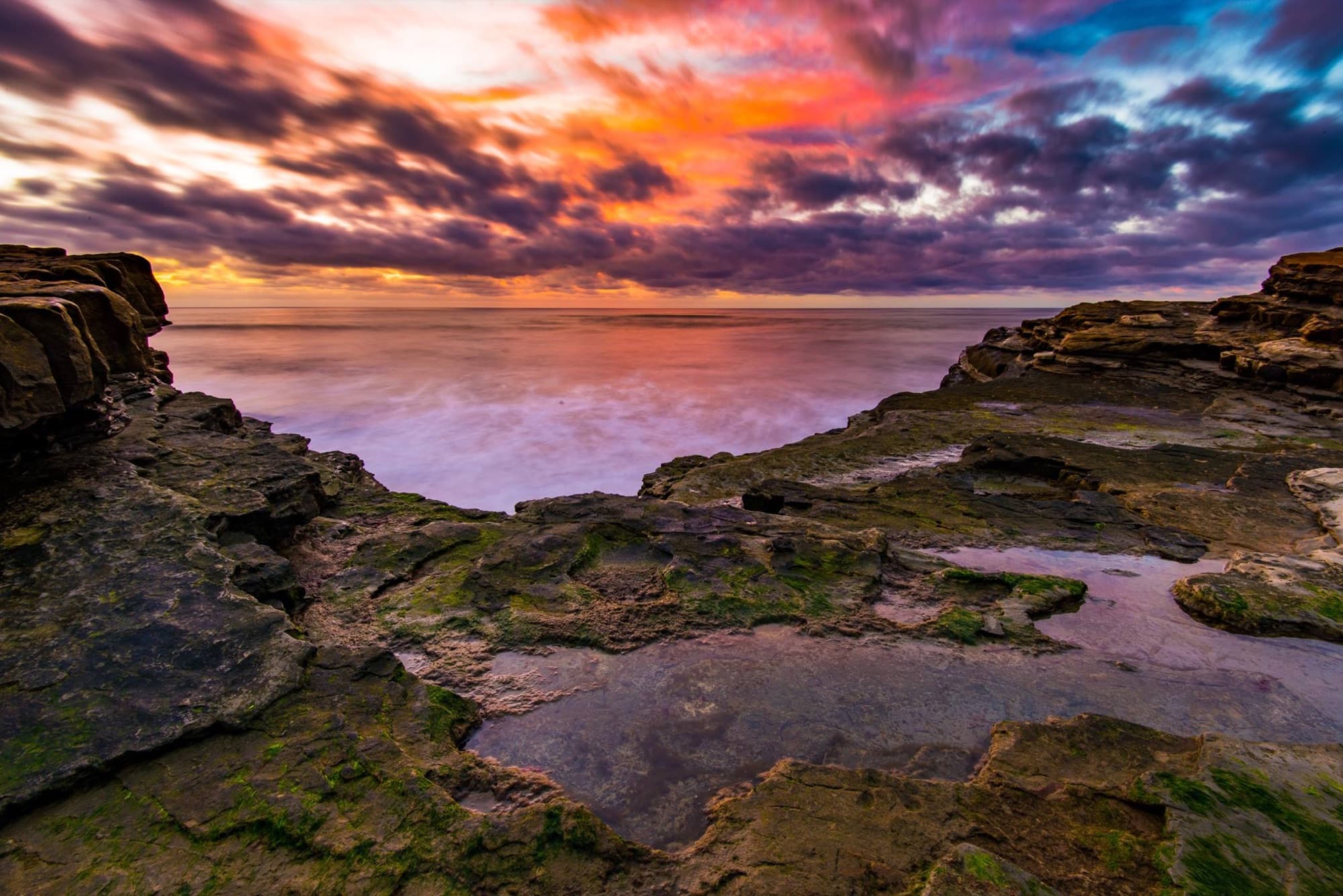 Rocky tide pools exposed at low tide reflecting a vivid orange and purple sunset at Cabrillo National Monument in San Diego