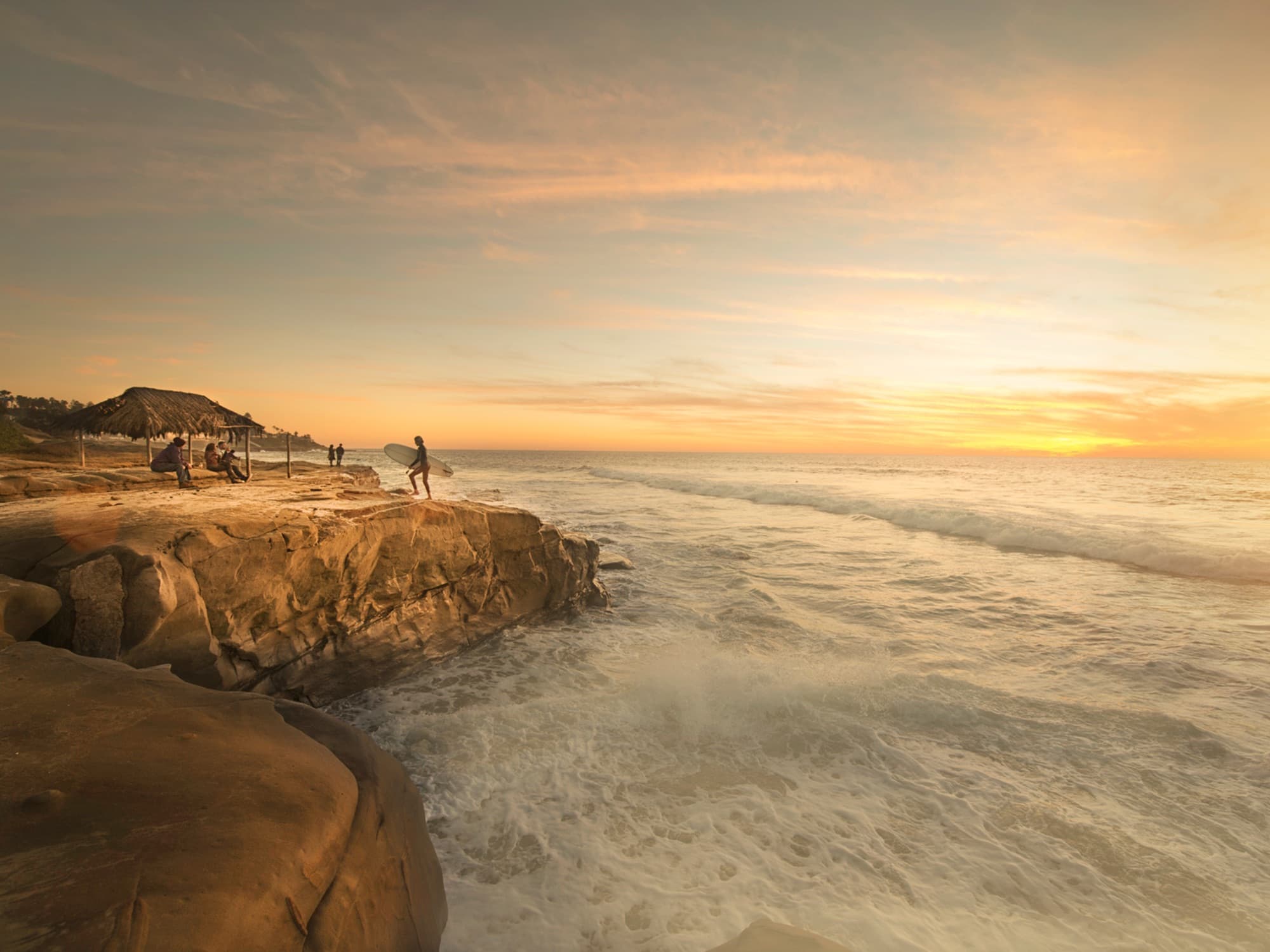 A surfer and friends gather on the sandstone bluffs at Windansea Beach in La Jolla as the sun sets over the Pacific