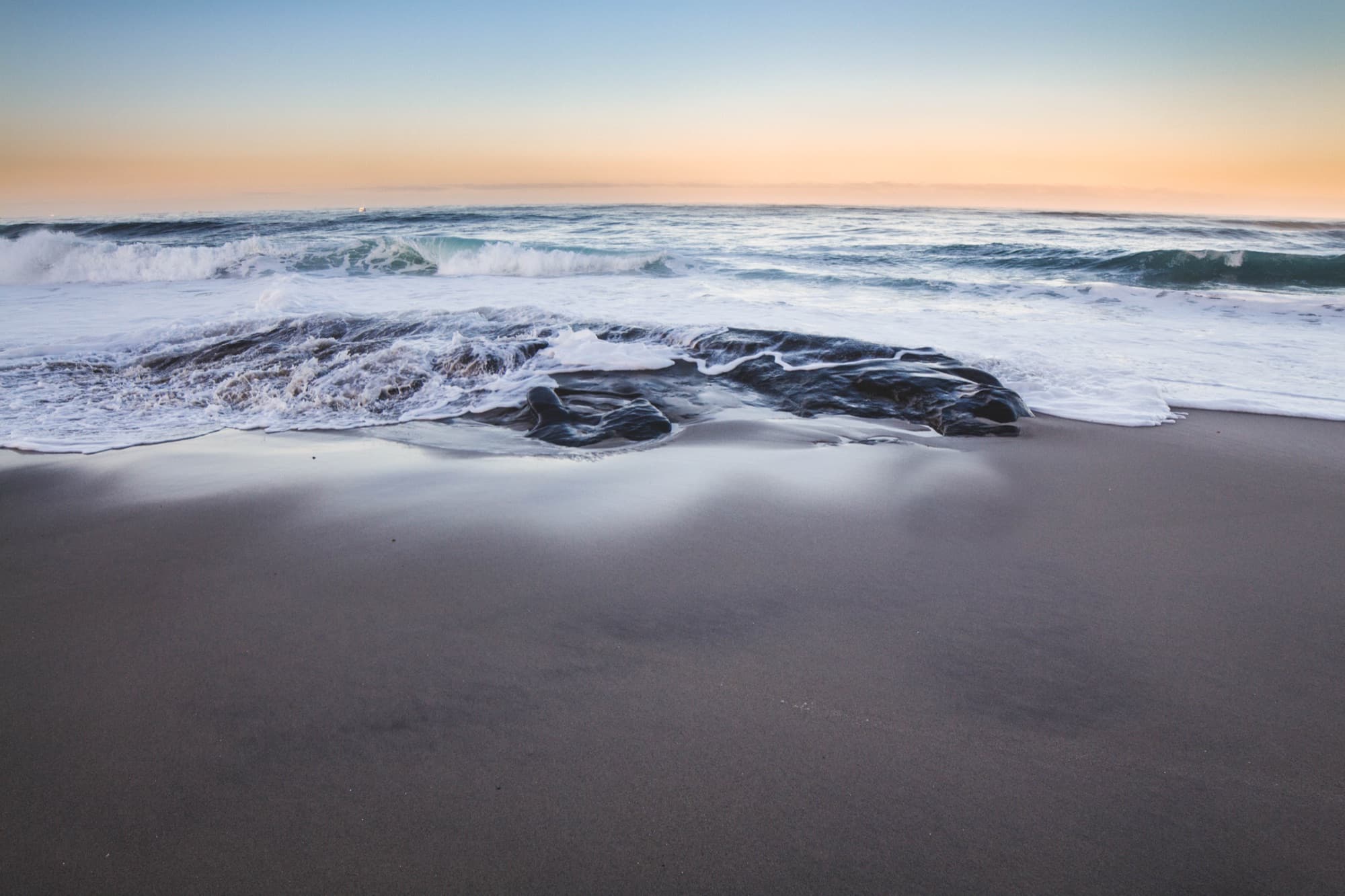 Foamy waves washing over smooth wet sand at dawn at Windansea Beach in La Jolla, San Diego