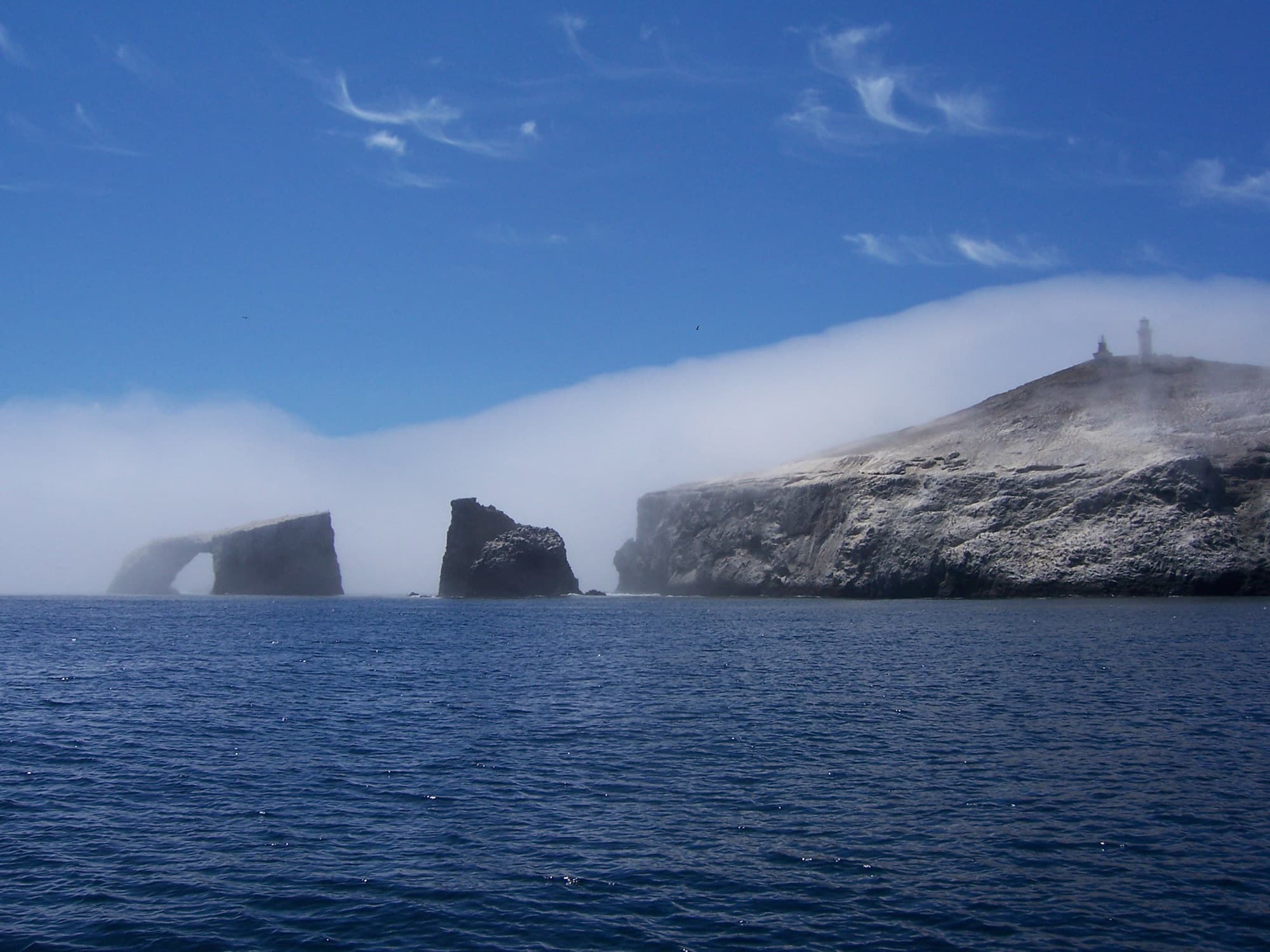 Anacapa Island's rock arch and lighthouse emerging from a bank of fog in Channel Islands National Marine Sanctuary