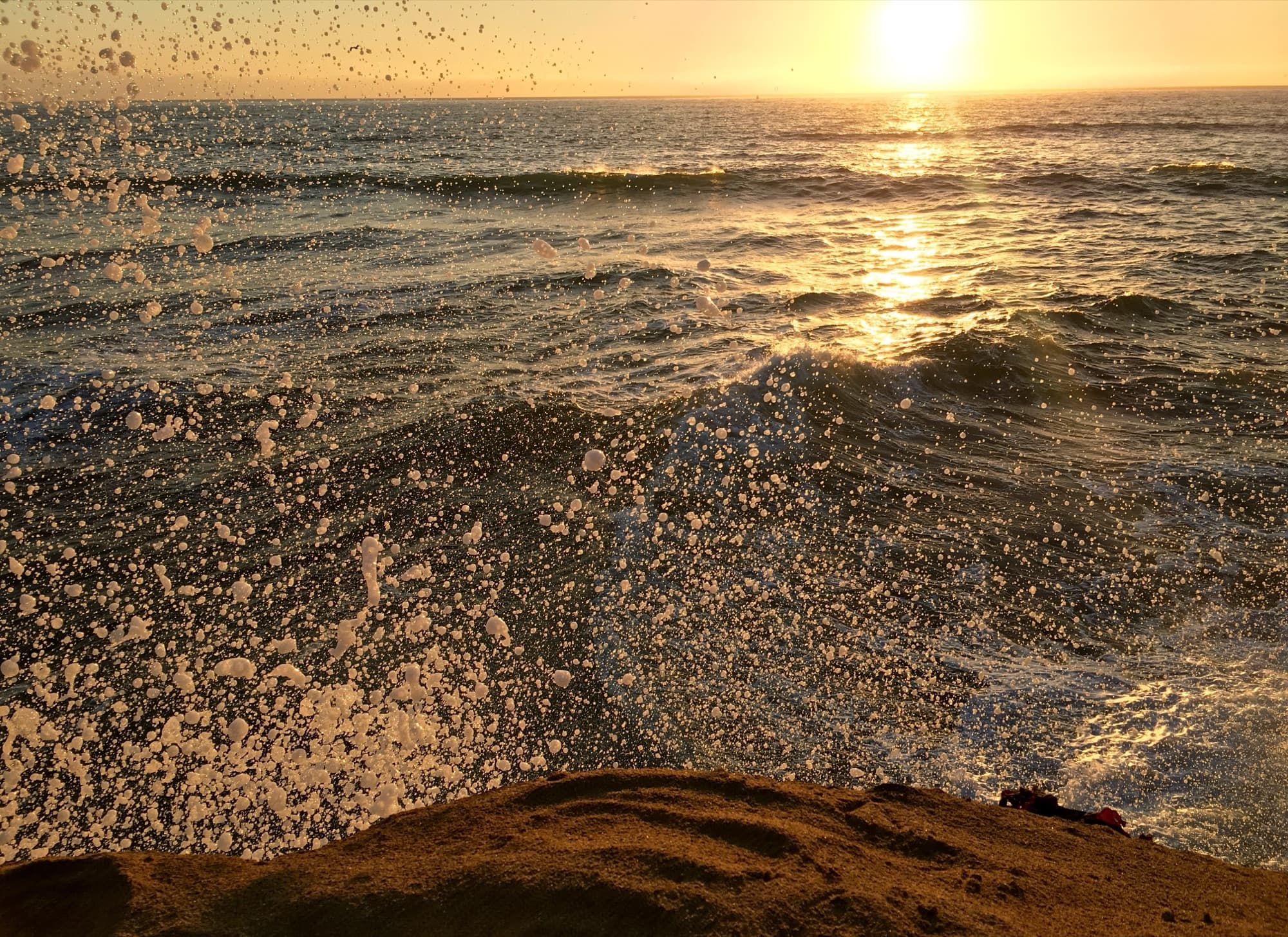 Golden sunset over the Pacific with sea spray flying above the sandstone bluffs at Sunset Cliffs in San Diego
