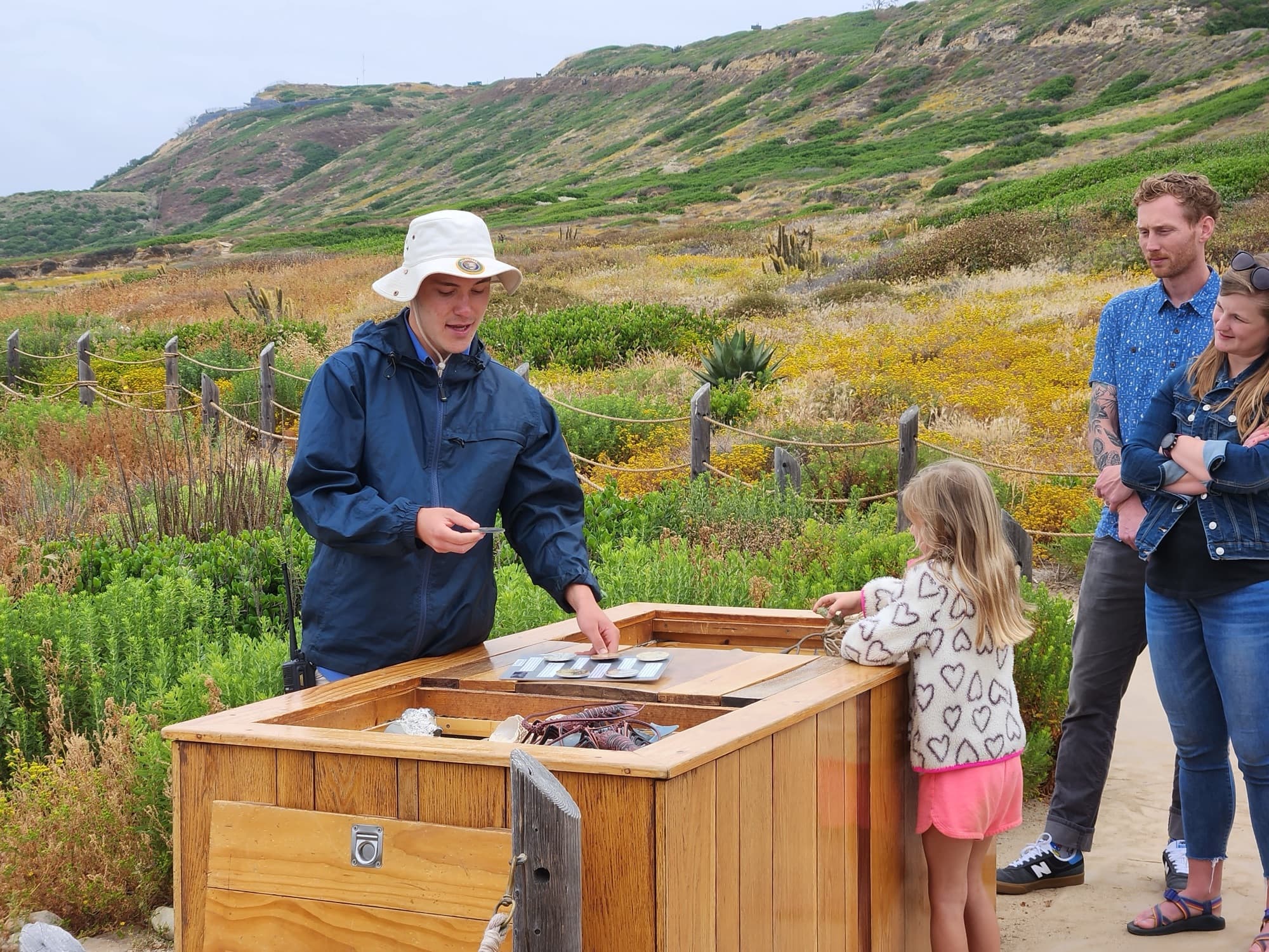 A park volunteer shows a young girl and her parents tide pool specimens at an outdoor education table at Cabrillo National Monument